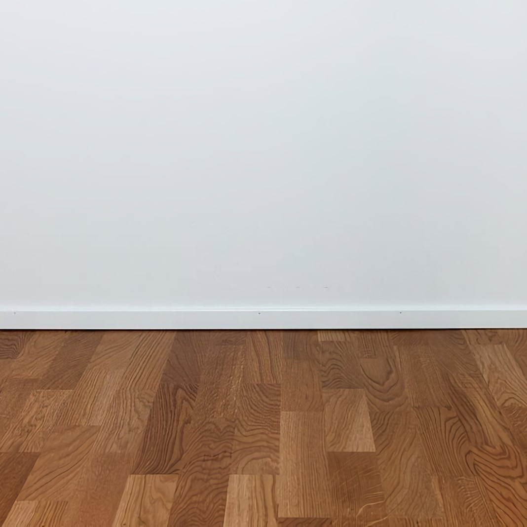 Wypolerowana, lakierowana podłoga parkietowa z drewna dębowego ułożona w jodełkę, widoczna przy białej ścianie z listwą przypodłogową.