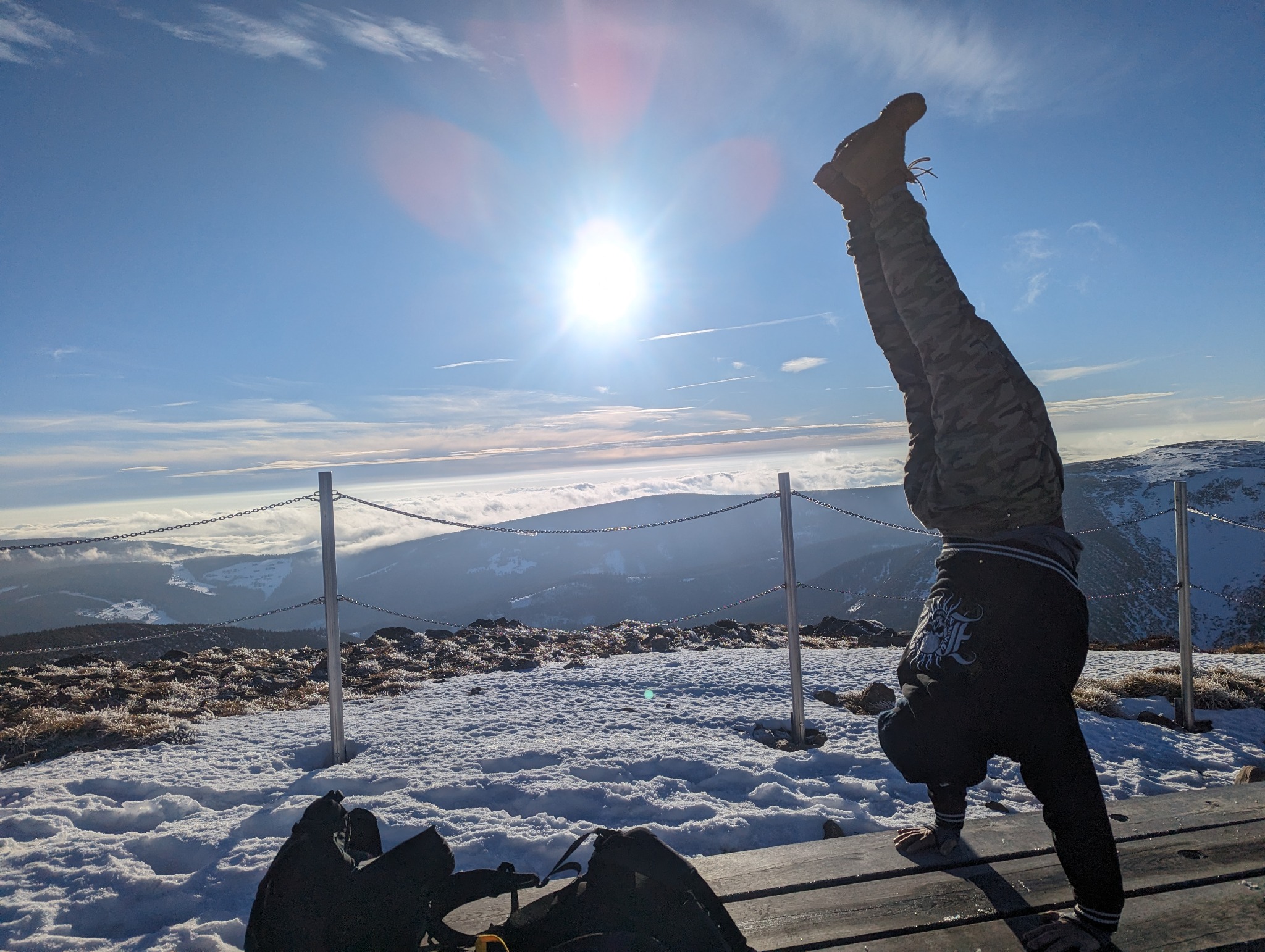Osoba w pozycji stania na rękach na tle górskiego krajobrazu z chmurami i błękitnym niebem. Akrobatyka na świeżym powietrzu w słoneczny dzień. Widok z góry.