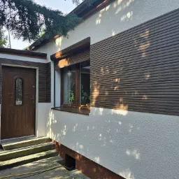 Elewacja domu z oknem z roletami zewnętrznymi i brązowymi panelami elewacyjnymi, widok z zewnątrz.