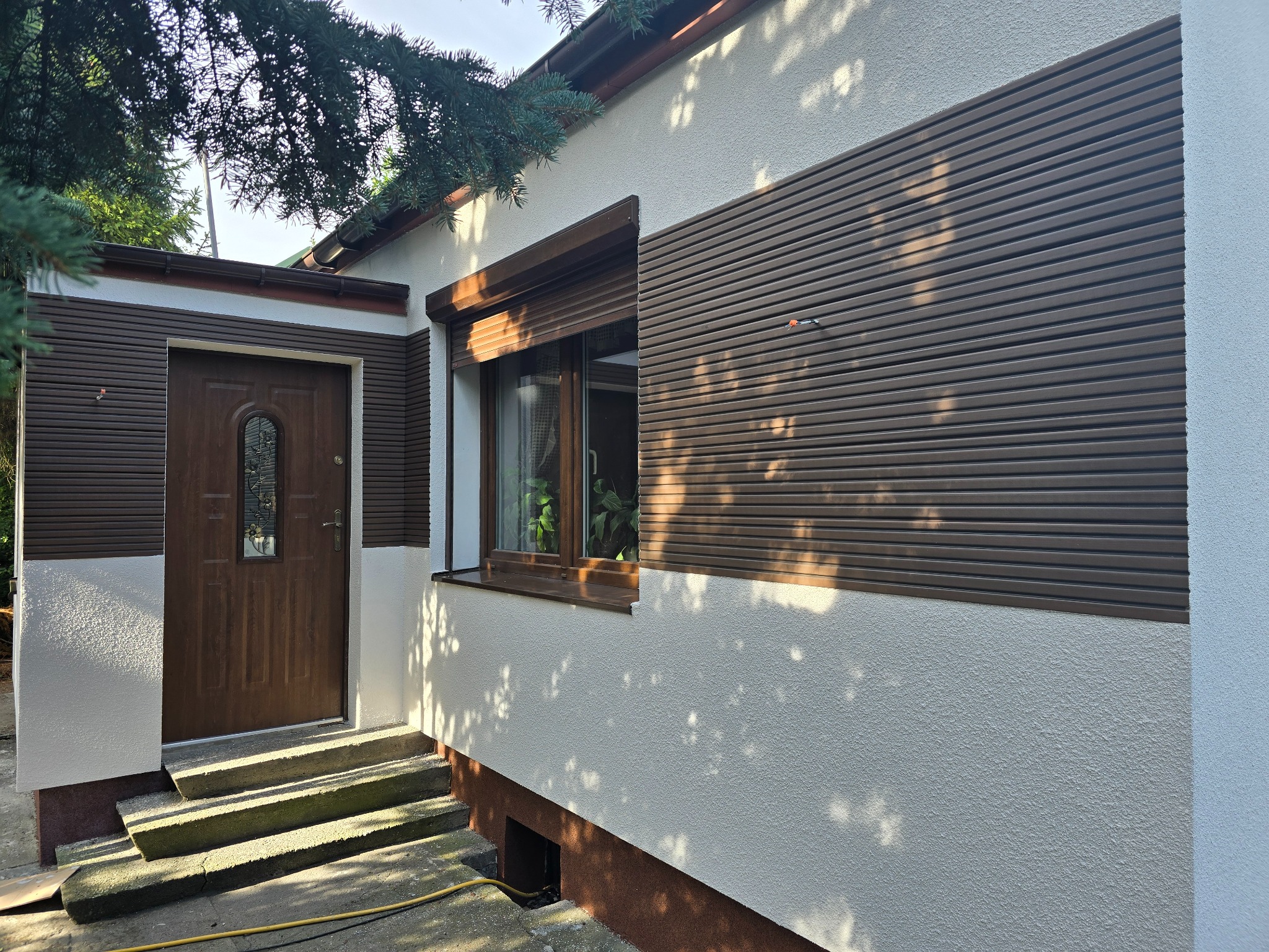 Elewacja domu z oknem z roletami zewnętrznymi i brązowymi panelami elewacyjnymi, widok z zewnątrz.