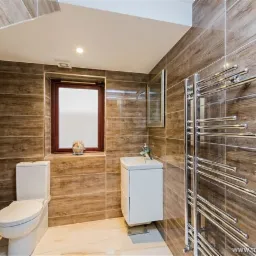 Nowoczesna łazienka z płytkami imitującymi drewno, białą ceramiką i grzejnikiem drabinkowym.