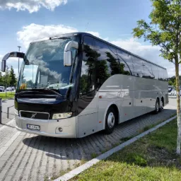 Srebrny autokar Volvo z czarnym przodem, zaparkowany na kostce brukowej obok trawnika z młodymi drzewkami, numer rejestracyjny SMI 34987.