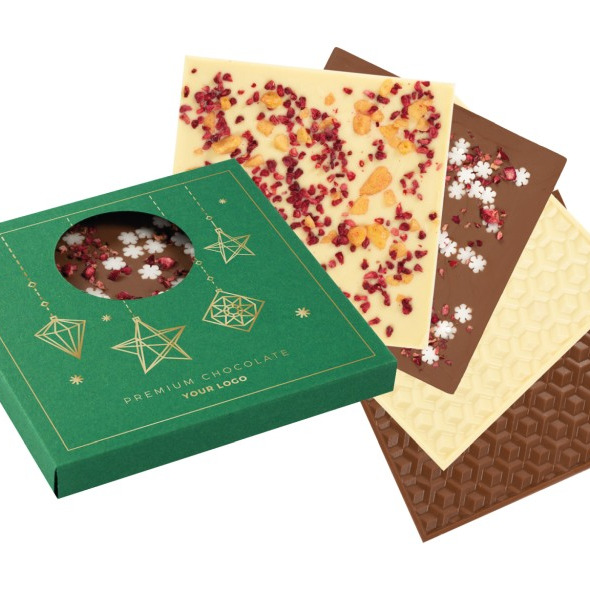Zestaw czekolad premium w ozdobnym, zielonym pudełku z okienkiem, eksponującym czekoladę wewnątrz, obok leżą tabliczki czekolady białej, mlecznej i gorzkiej z różnymi posypkami i wzorami.