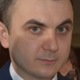 Portret młodego mężczyzny w ciemnym garniturze i białej koszuli z krawatem, z bliska, z zielonymi oczami.