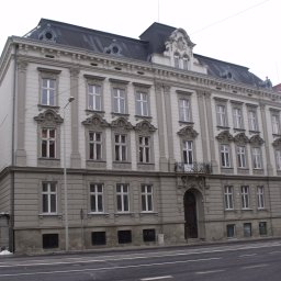 INWESTPROJEKT - Elewacja odnowionego, trzypiętrowego budynku w stylu klasycystycznym z ozdobnymi detalami architektonicznymi, widziana z perspektywy ulicy w pochmurny dzień.