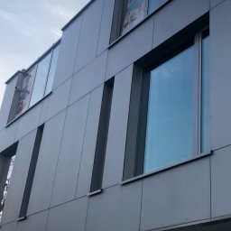 MW CLEANING MATEUSZ WIECZOREK - Nowoczesny budynek biurowy z szarej elewacji panelowej i dużymi oknami odbijającymi niebieskie niebo.
