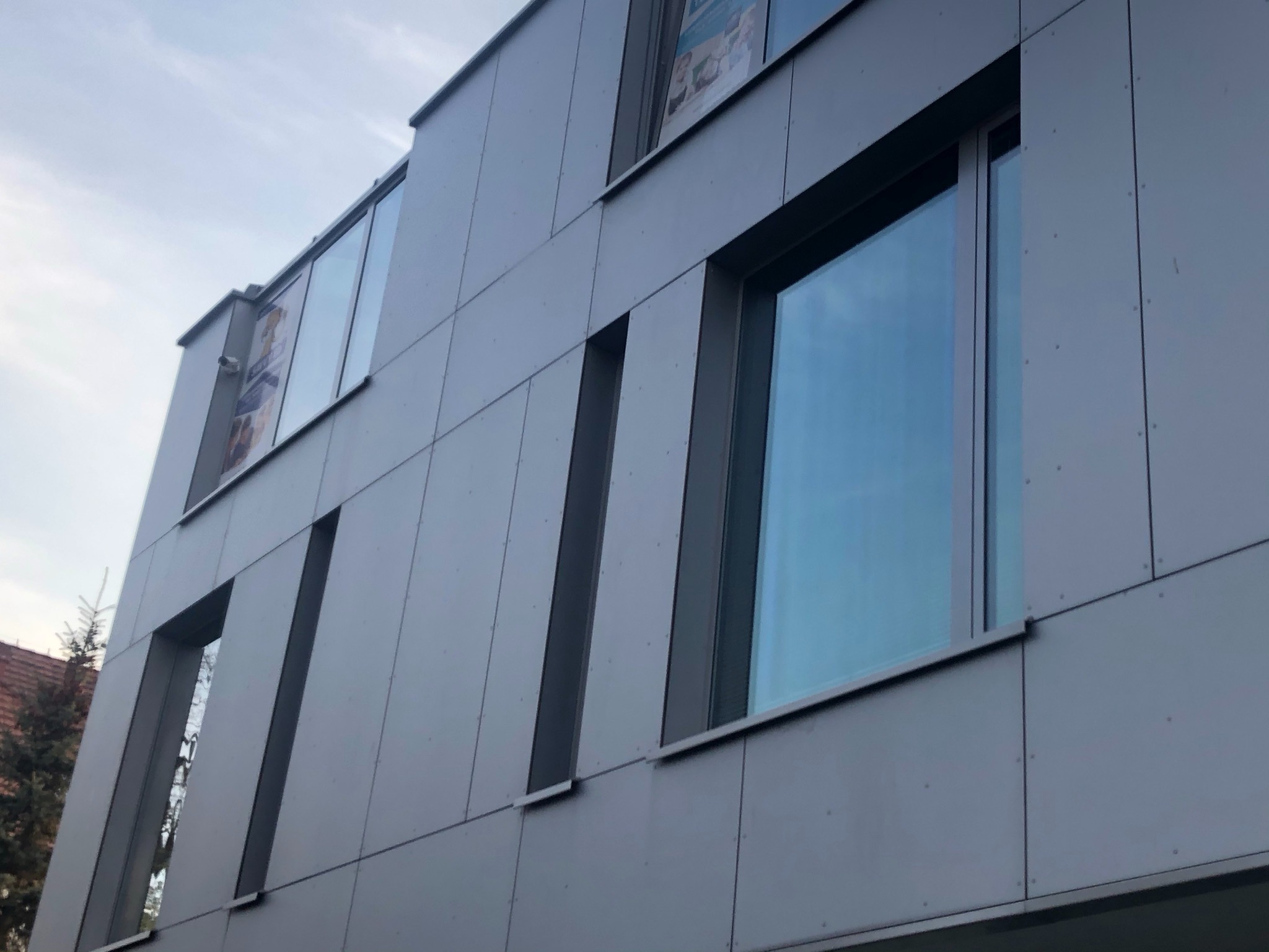 Nowoczesny budynek biurowy z szarej elewacji panelowej i dużymi oknami odbijającymi niebieskie niebo.