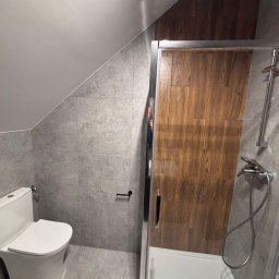 My Way - Ośrodek leczenia uzależnień - Szara łazienka na poddaszu ze skośnym sufitem, z toaletą i kabiną prysznicową z drewnopodobnymi drzwiami. Widoczna wentylacja.