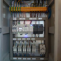 KNM inż. Mateusz Kyrcz - Wnętrze szafy sterowniczej z modułami elektronicznymi, złączkami, przewodami i gniazdem 230V, widoczne diody LED i etykiety opisujące komponenty.