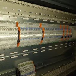 Szyna DIN z zamontowanymi listwami zaciskowymi z numeracją, widok z góry pod kątem, oświetlenie techniczne.