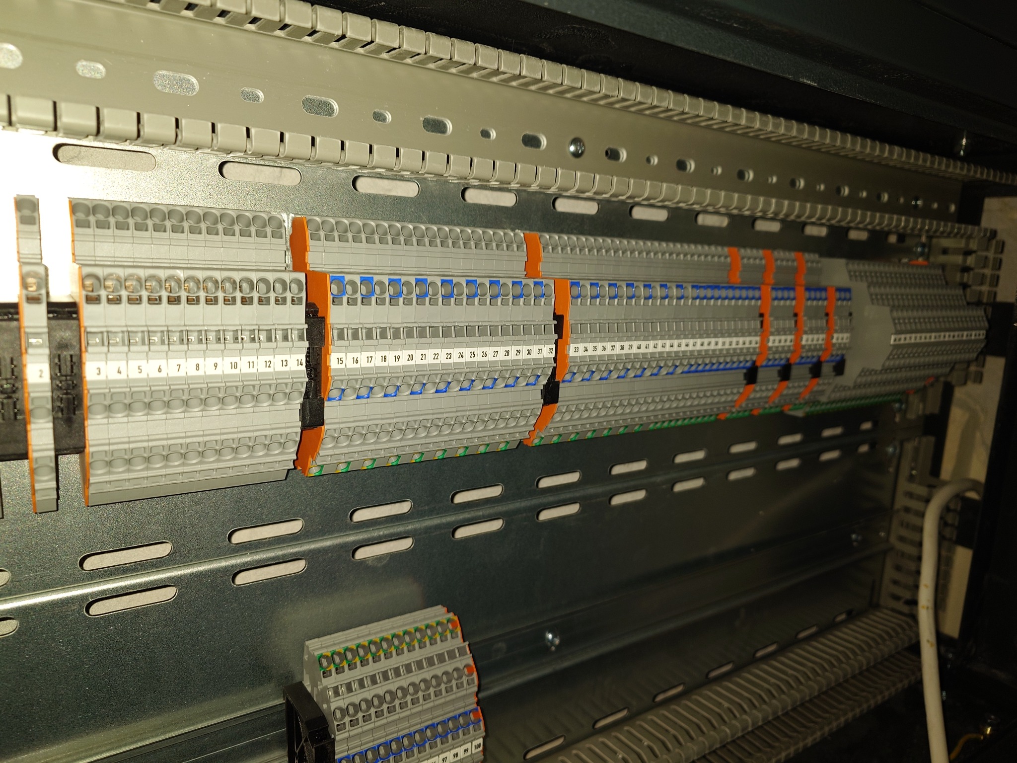 Szyna DIN z zamontowanymi listwami zaciskowymi z numeracją, widok z góry pod kątem, oświetlenie techniczne.