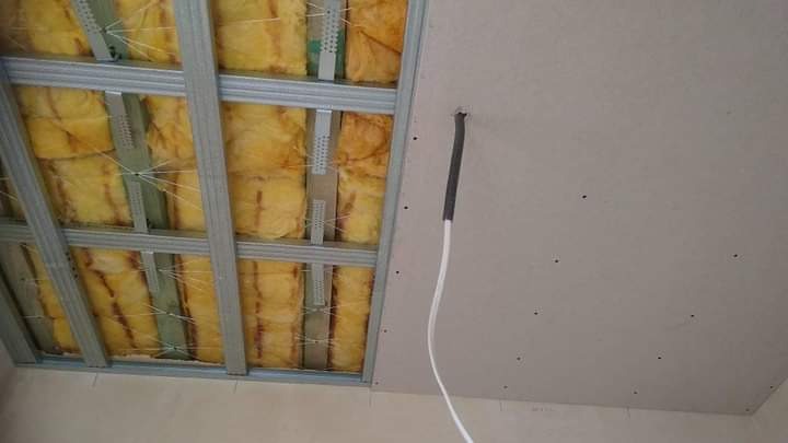 Montaż sufitu podwieszanego z widoczną izolacją z wełny mineralnej i wystającym przewodem elektrycznym w peszlu.