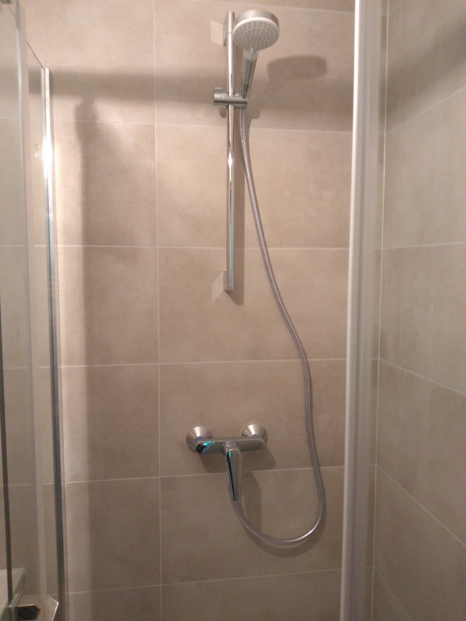 Szczegółowy widok kabiny prysznicowej z beżowymi płytkami, chromowaną baterią i słuchawką prysznicową, widoczne uszczelki kabiny.