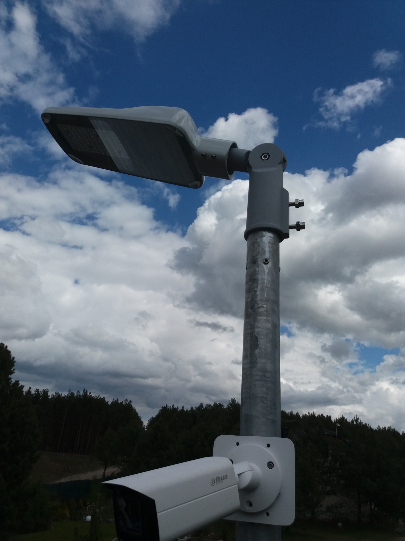 Słup oświetleniowy LED z zamontowaną kamerą monitoringu Dahua na tle błękitnego nieba z obłokami.
