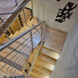 F.H.U. TreeBiel Piotr Bielak - Nowoczesne schody z jasnego drewna z metalową balustradą, widok z góry. Na ścianie dekoracja w kształcie gałęzi i oświetlenie punktowe.