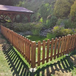 F.H.U. TreeBiel Piotr Bielak - Nowoczesne ogrodzenie z drewna otaczające oczko wodne w ogrodzie. W tle altana i bujna roślinność. Wyraźne cienie rzucane przez płot na trawnik.