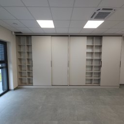 F.H.U. TreeBiel Piotr Bielak - Szafa na wymiar z przesuwnymi drzwiami i półkami w Nowym Sączu. Jasne wnętrze, minimalistyczny design, widok z okna na zewnątrz. Nowoczesne rozwiązanie do przechowywania.