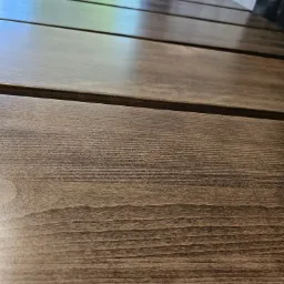 Zbliżenie na fragment drewnianego tarasu z widocznym usłojeniem drewna i refleksami światła na lakierowanej powierzchni desek.