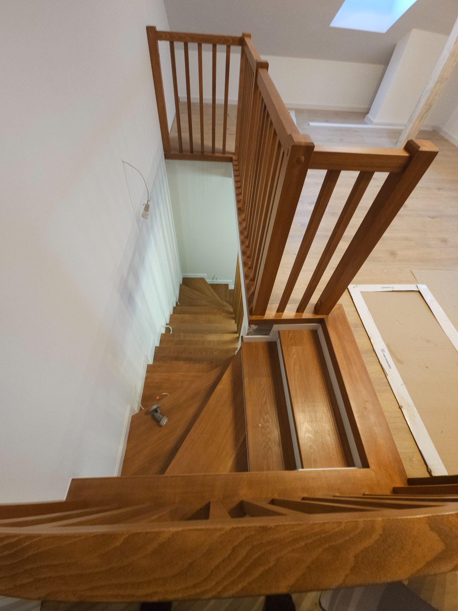 Drewniane schody z balustradą, widok z góry. Na jednym ze stopni leży wkrętarka. Widoczne niedociągnięcia wykończeniowe.