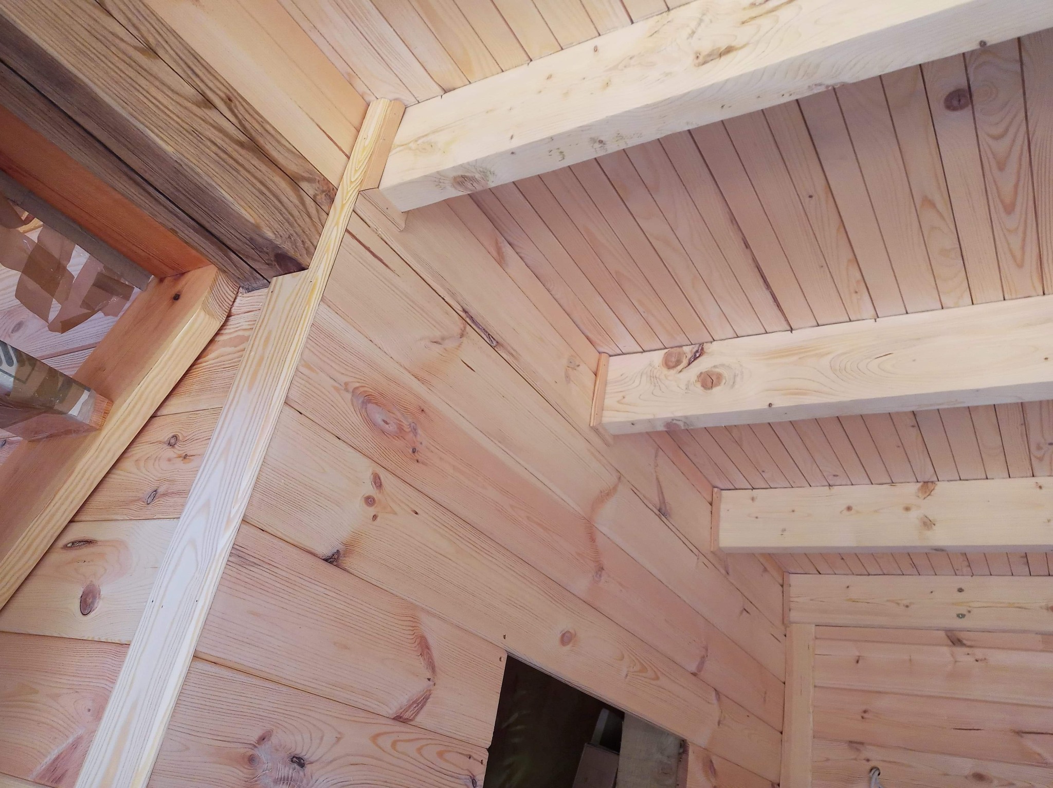 Fragment poddasza wykończonego jasnym drewnem z widocznymi elementami konstrukcyjnymi i oknem dachowym w trakcie prac wykończeniowych.