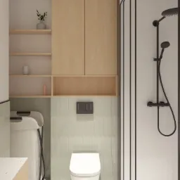 Wizualizacja łazienki z kabiną prysznicową w czarnej ramie, podwieszaną toaletą, szafkami z jasnego drewna i otwartymi półkami z dekoracjami, wykończona płytkami w odcieniach bieli i zieleni.