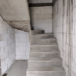 Usługi Ciesielsko-Budowlane DAR-BUD Dariusz Czerwiński - Surowe betonowe schody wewnątrz budynku w trakcie budowy, ściany z białych bloczków, widoczne ślady po zaprawie, surowy stan wykończenia.