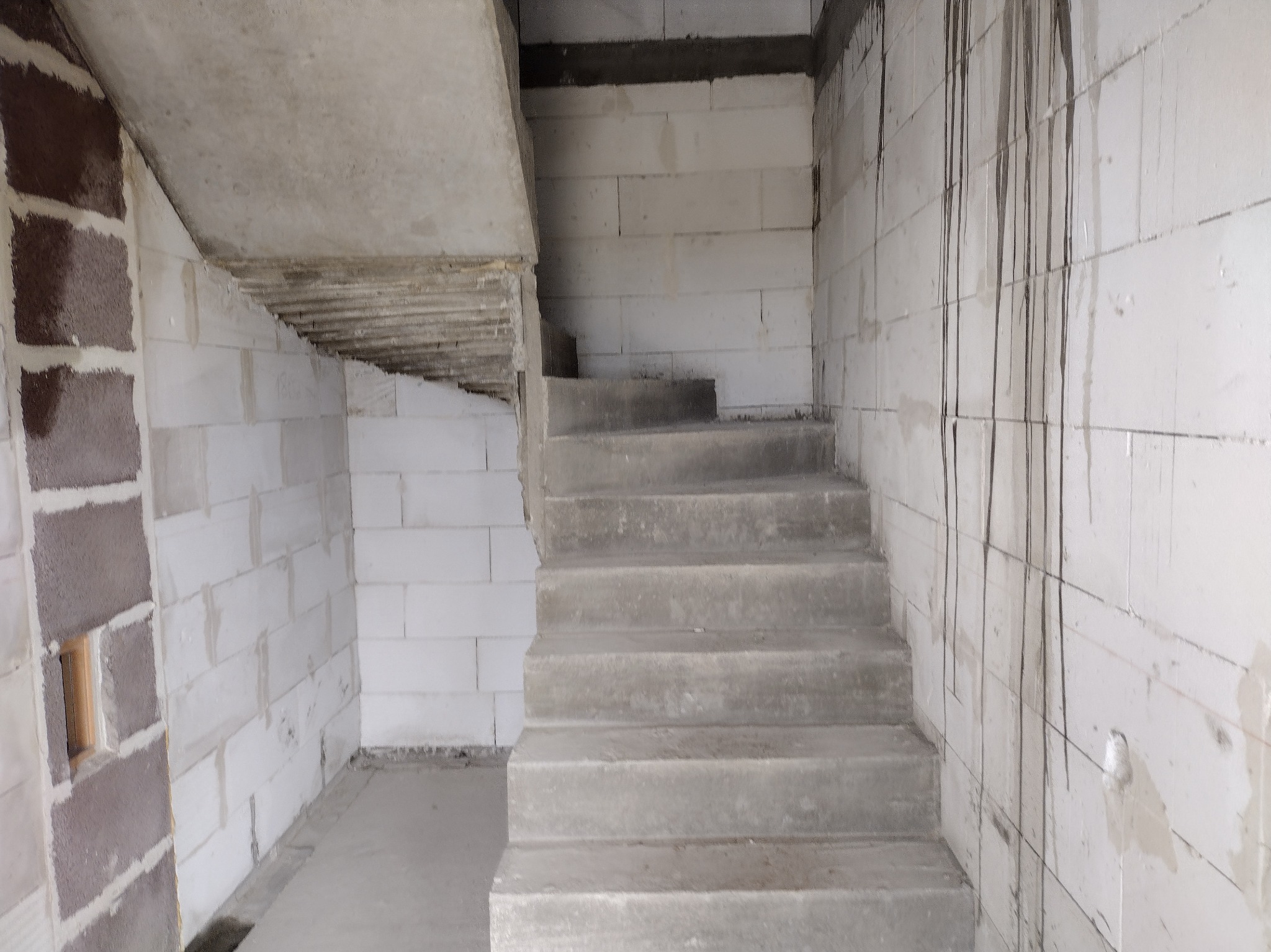 Surowe betonowe schody wewnątrz budynku w trakcie budowy, ściany z białych bloczków, widoczne ślady po zaprawie, surowy stan wykończenia.