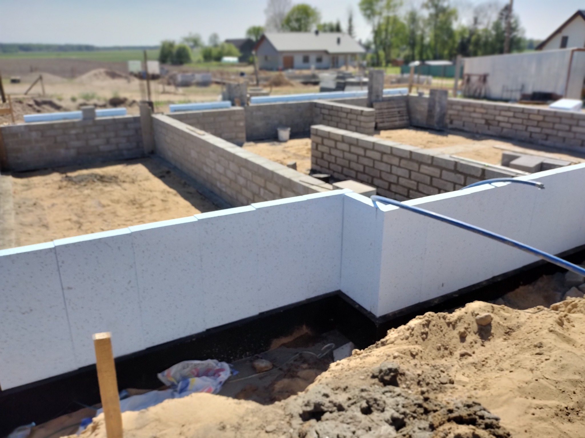 Fundamenty domu w trakcie budowy: ściany z bloczków betonowych i izolacja termiczna z białego styropianu. Widok na plac budowy w słoneczny dzień.