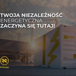 Dom Niskoemisyjny - Grafika reklamowa prezentująca magazyn energii z żółtym symbolem błyskawicy na tle farmy fotowoltaicznej i turbin wiatrowych, z hasłem 'Twoja niezależność energetyczna zaczyna się tutaj!' i logo...