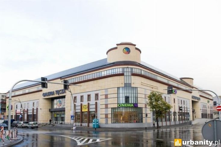 Widok na budynek Galerii Tęcza z ulicy w pochmurny dzień, z widocznym skrzyżowaniem i sygnalizacją świetlną.