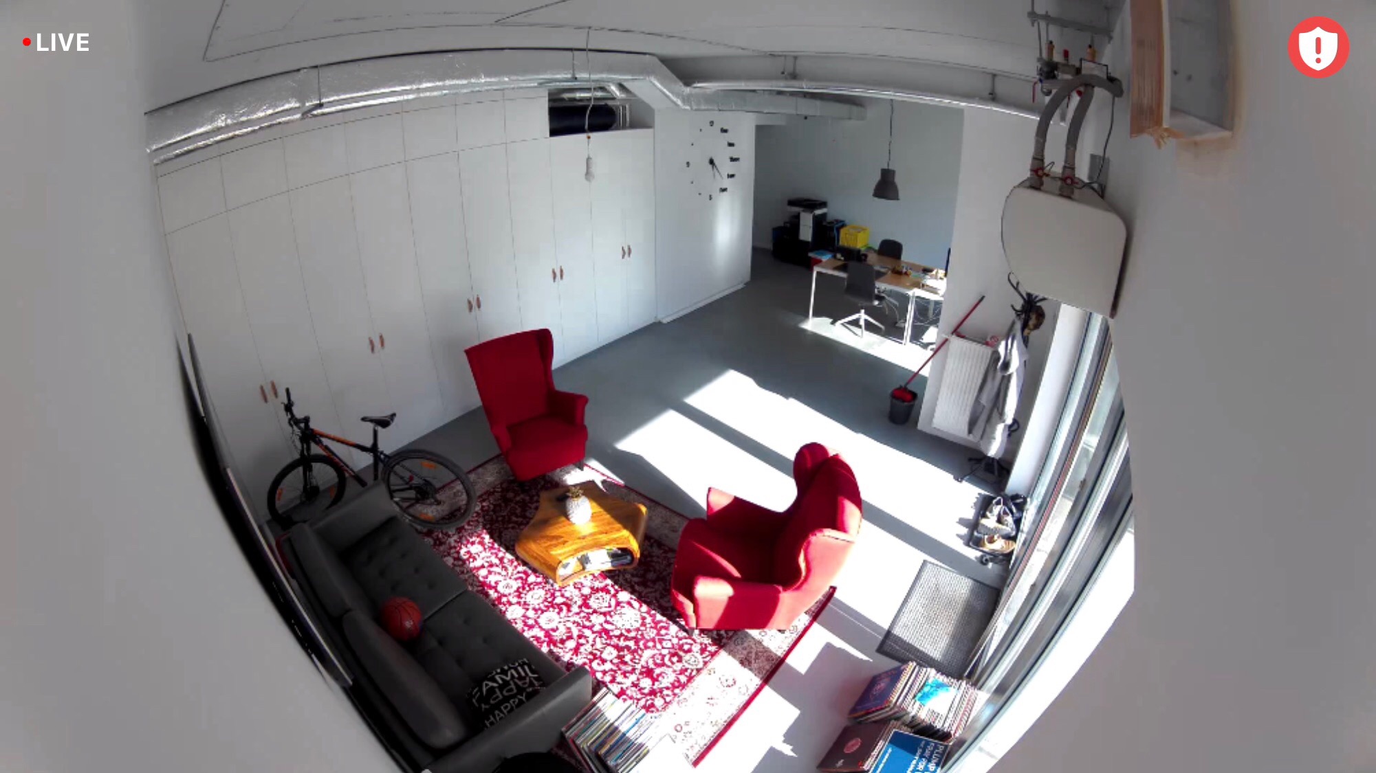 Wnętrze biura IKS w Warszawie z widoczną konstrukcją stalową stropu, białymi szafami w zabudowie, dwoma czerwonymi fotelami, szarą kanapą, rowerem i biurkiem w oddali.