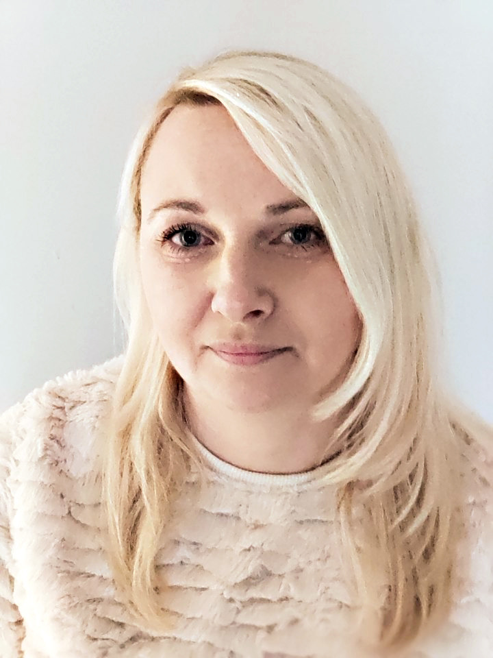 Portret blondwłosej kobiety w swetrze z fakturą, na jasnym tle.