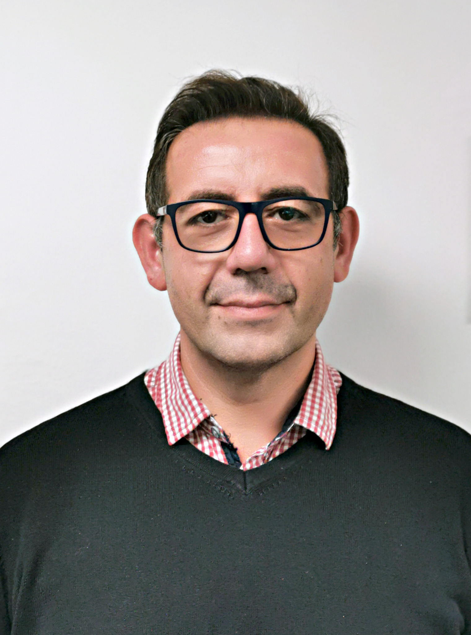 Portret mężczyzny w okularach, ubrany w czarny sweter i koszulę w czerwoną kratę, na białym tle.