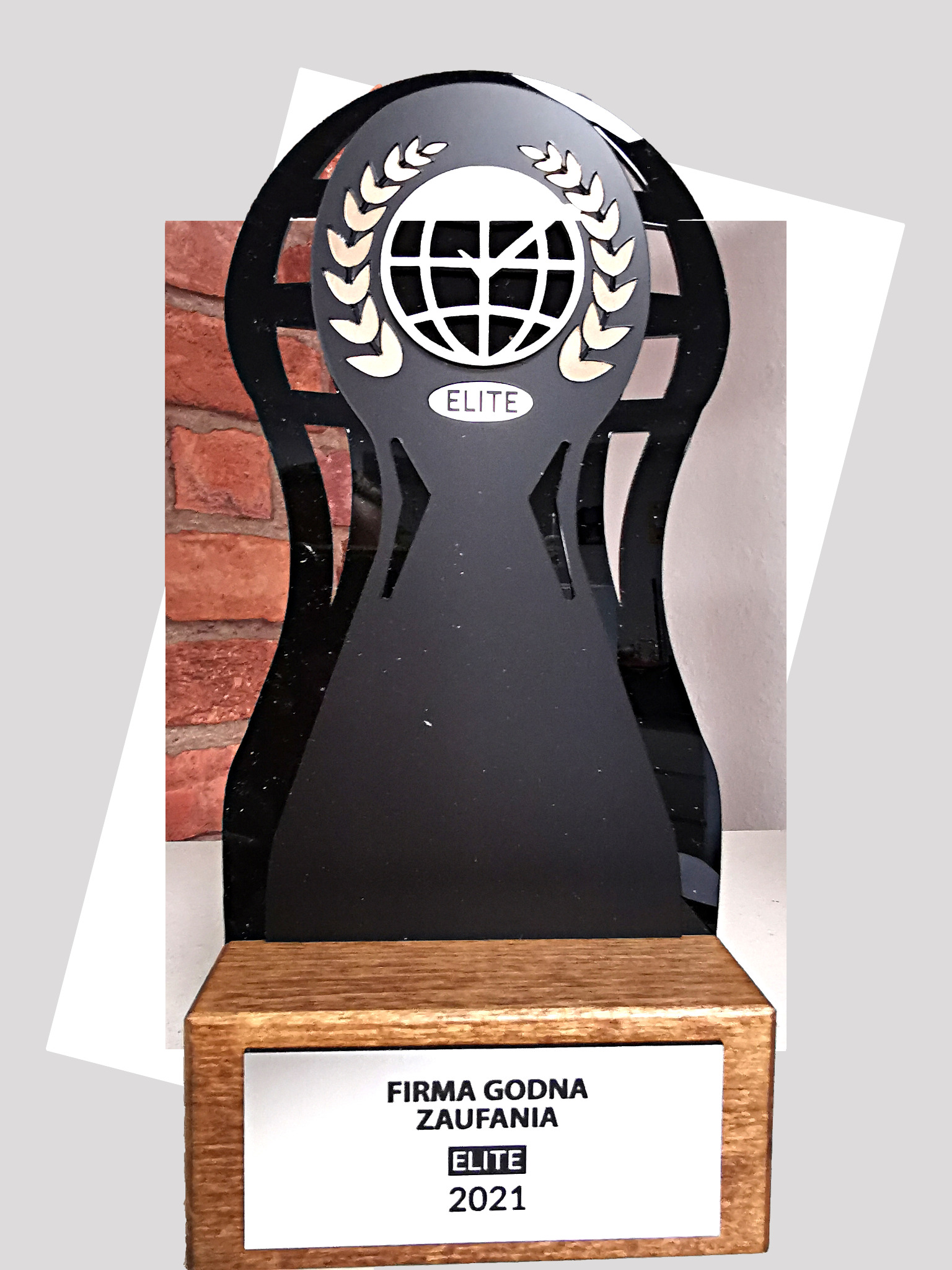 Nagroda 'Firma Godna Zaufania ELITE 2021' z czarnego akrylu na drewnianej podstawie, z symbolem globu otoczonego laurem