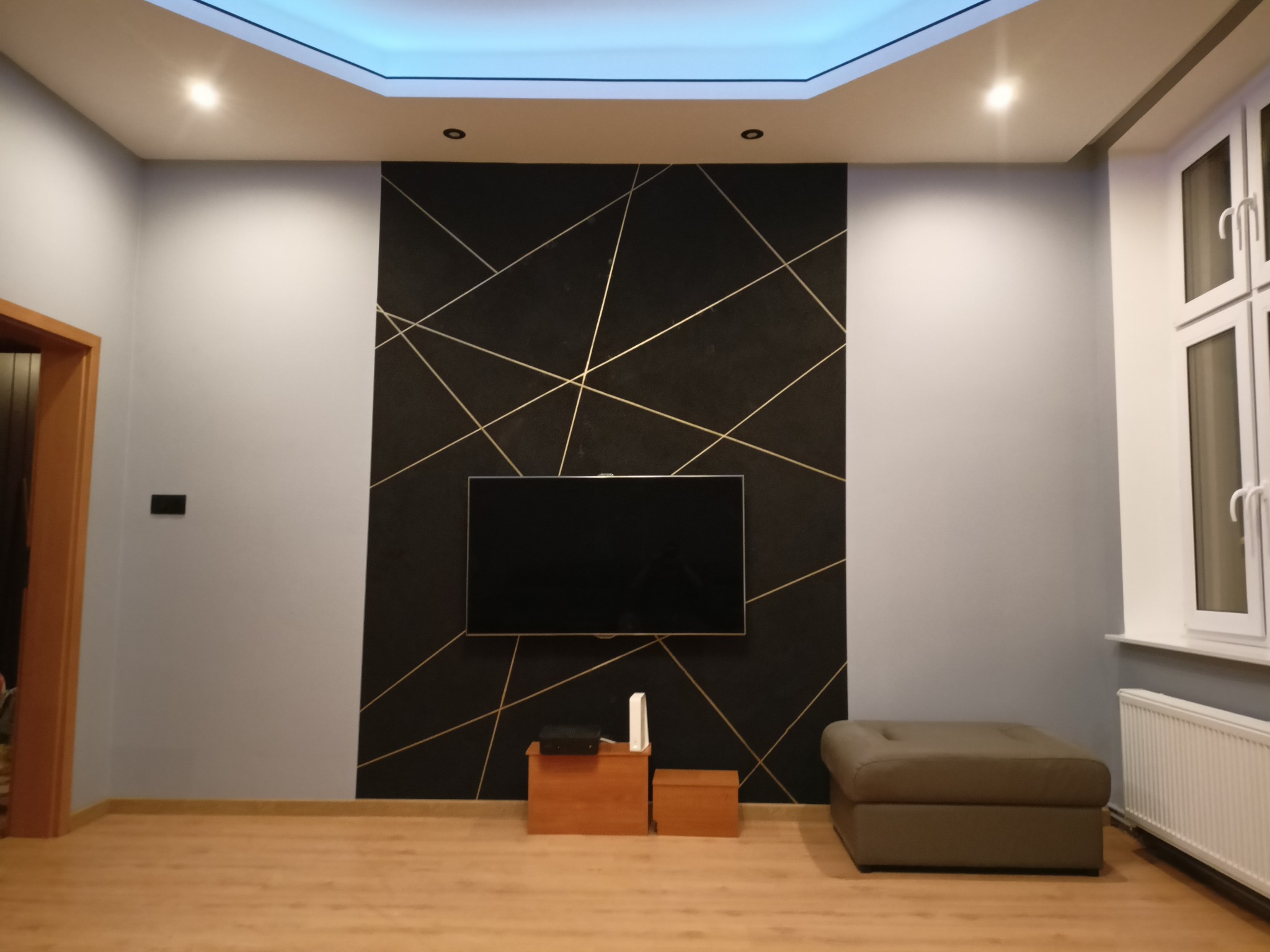 Salon po metamorfozie: czarna ściana akcentowa z geometrycznym, złotym wzorem, podwieszany sufit z oświetleniem LED. Nowoczesny design wnętrza.