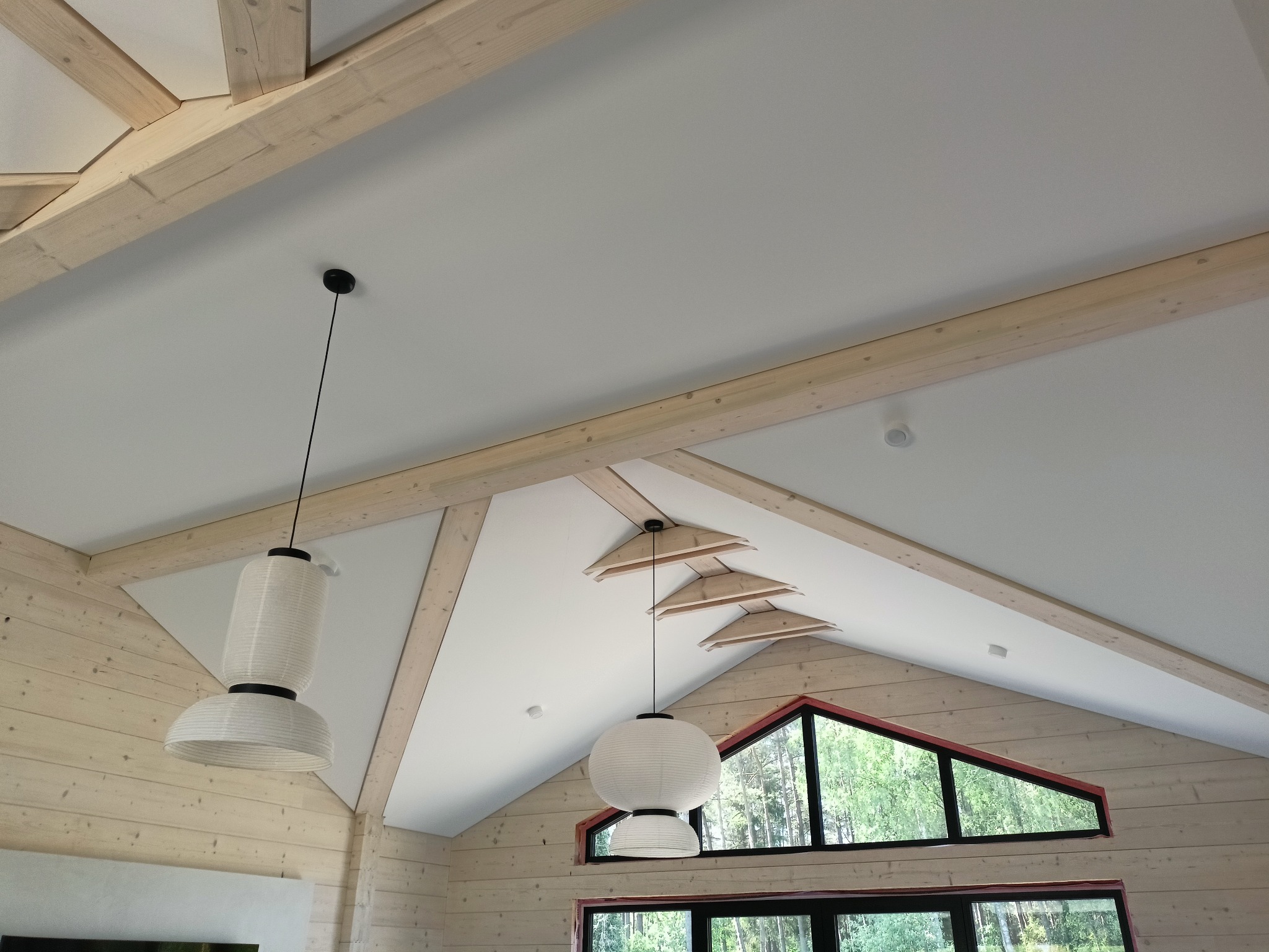 Jasne drewno i biel: nowoczesne wykończenie wnętrza z belkami stropowymi, lampami wiszącymi i oknami z widokiem na zieleń. Minimalistyczny design.