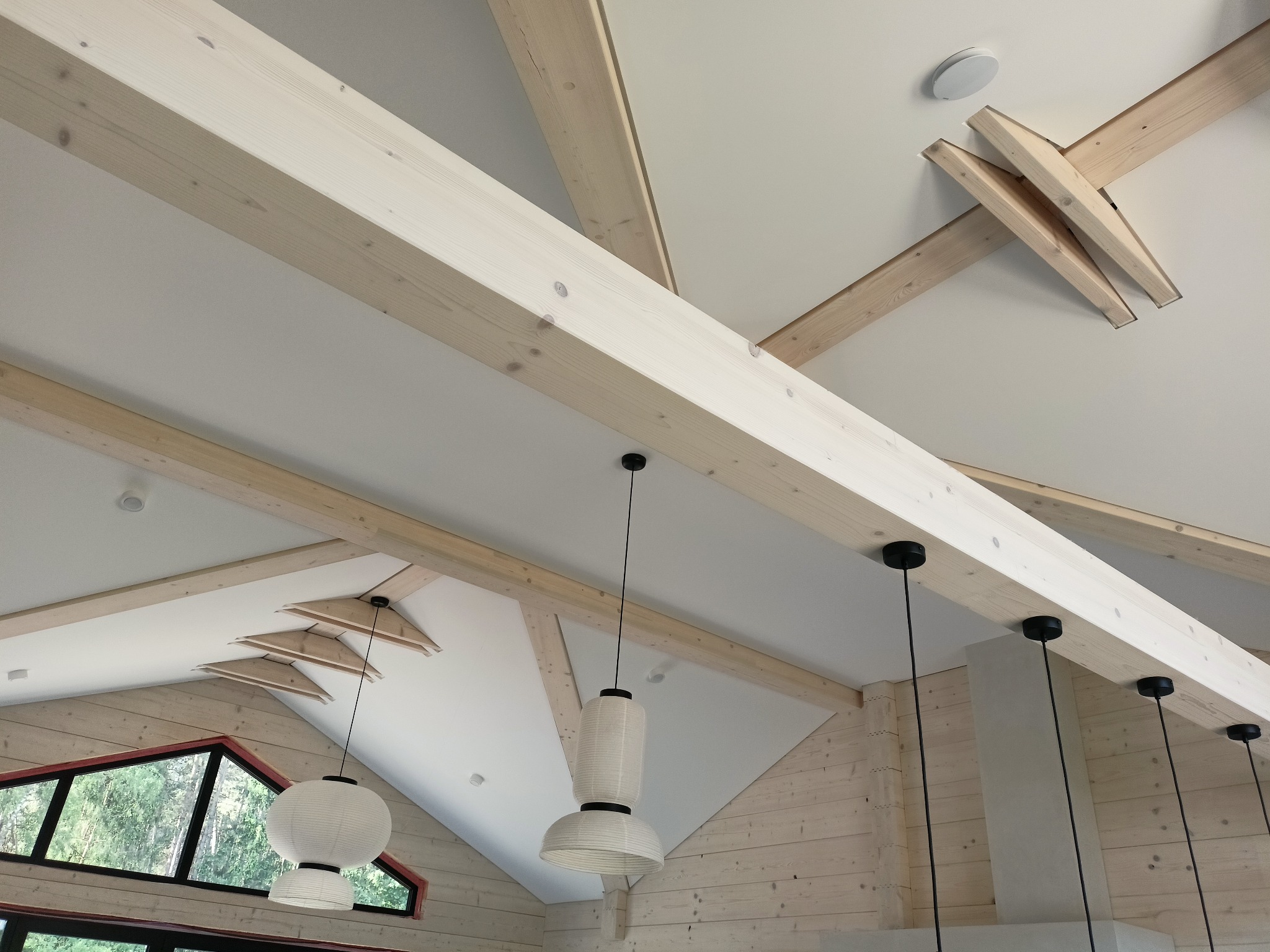 Jasne drewniane belki stropowe i lampy wiszące w nowoczesnym wnętrzu. Widok z dołu na sufit z elementami drewnianymi i oświetleniem.
