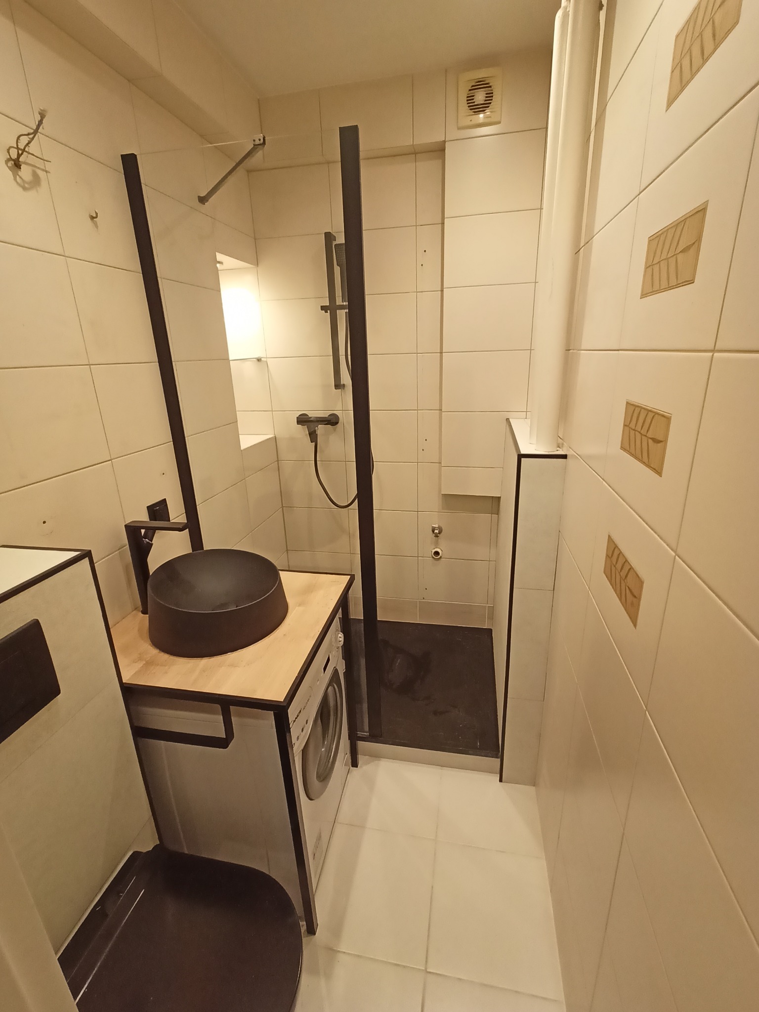 Nowoczesna łazienka z czarną armaturą, umywalką nablatową i kabiną prysznicową typu walk-in, pralka zabudowana pod blatem umywalki.