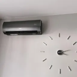 Czarny klimatyzator marki Gree zamontowany na jasnej ścianie w pokoju, obok dekoracyjny zegar ścienny.