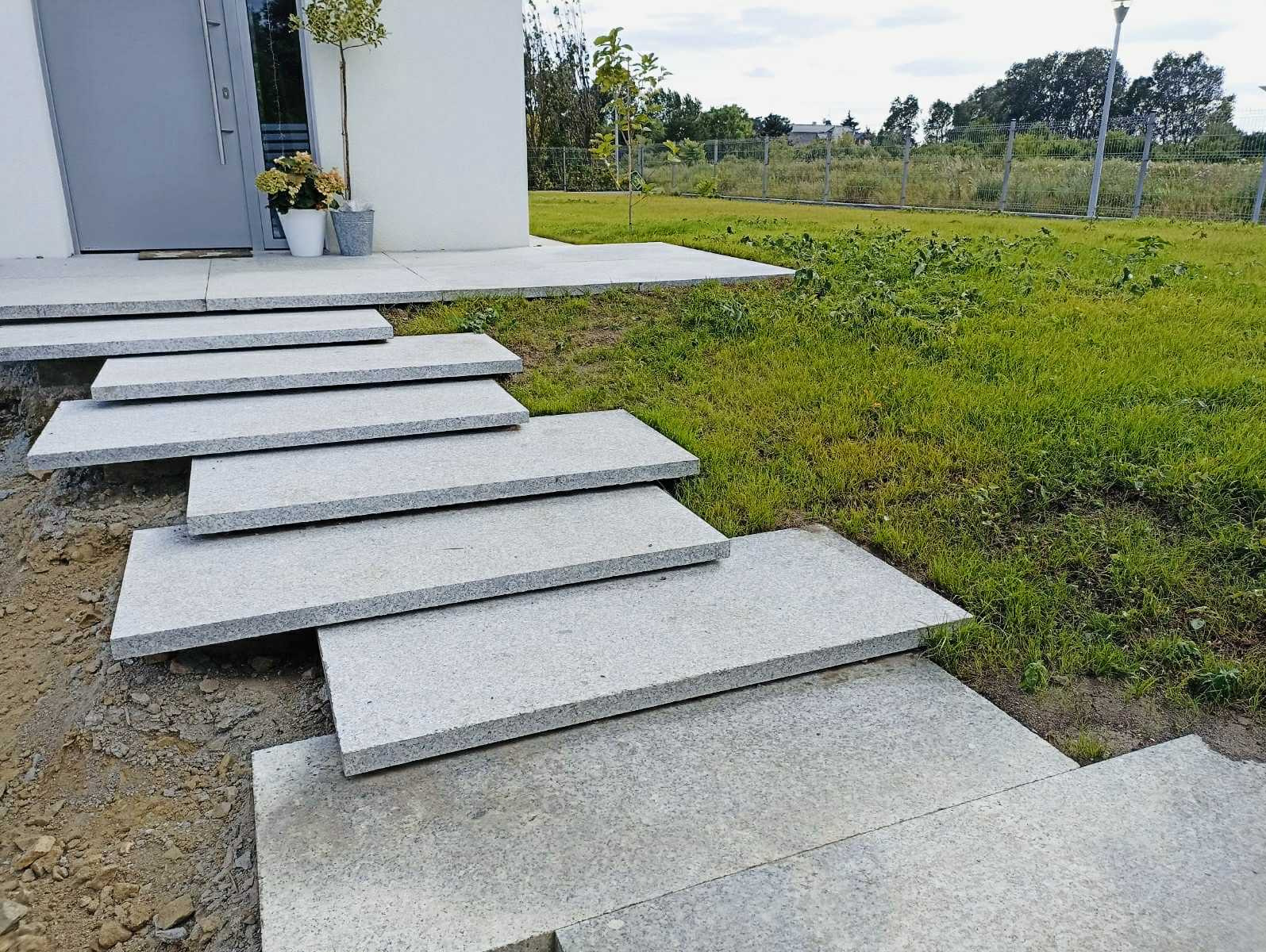 Granitowe stopnie prowadzące do domu, otoczone zielonym trawnikiem. Minimalistyczny design, jasne kolory, nowoczesna architektura. Widok z dołu, podkreślający fakturę kamienia.