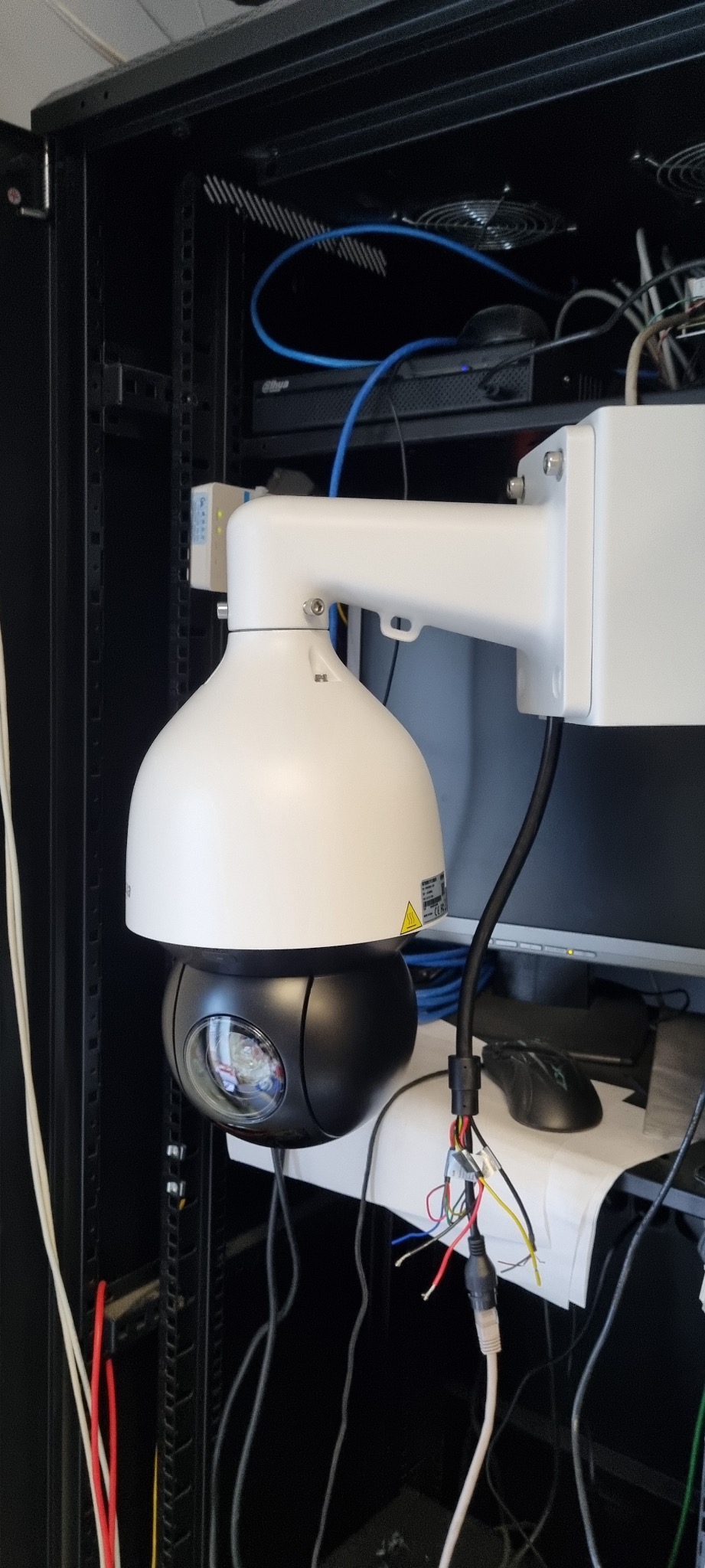 Kamera PTZ Dahua zamontowana w szafie rack, widoczne okablowanie i elementy sieciowe. Detaliczny widok na instalację systemu monitoringu wizyjnego w serwerowni.