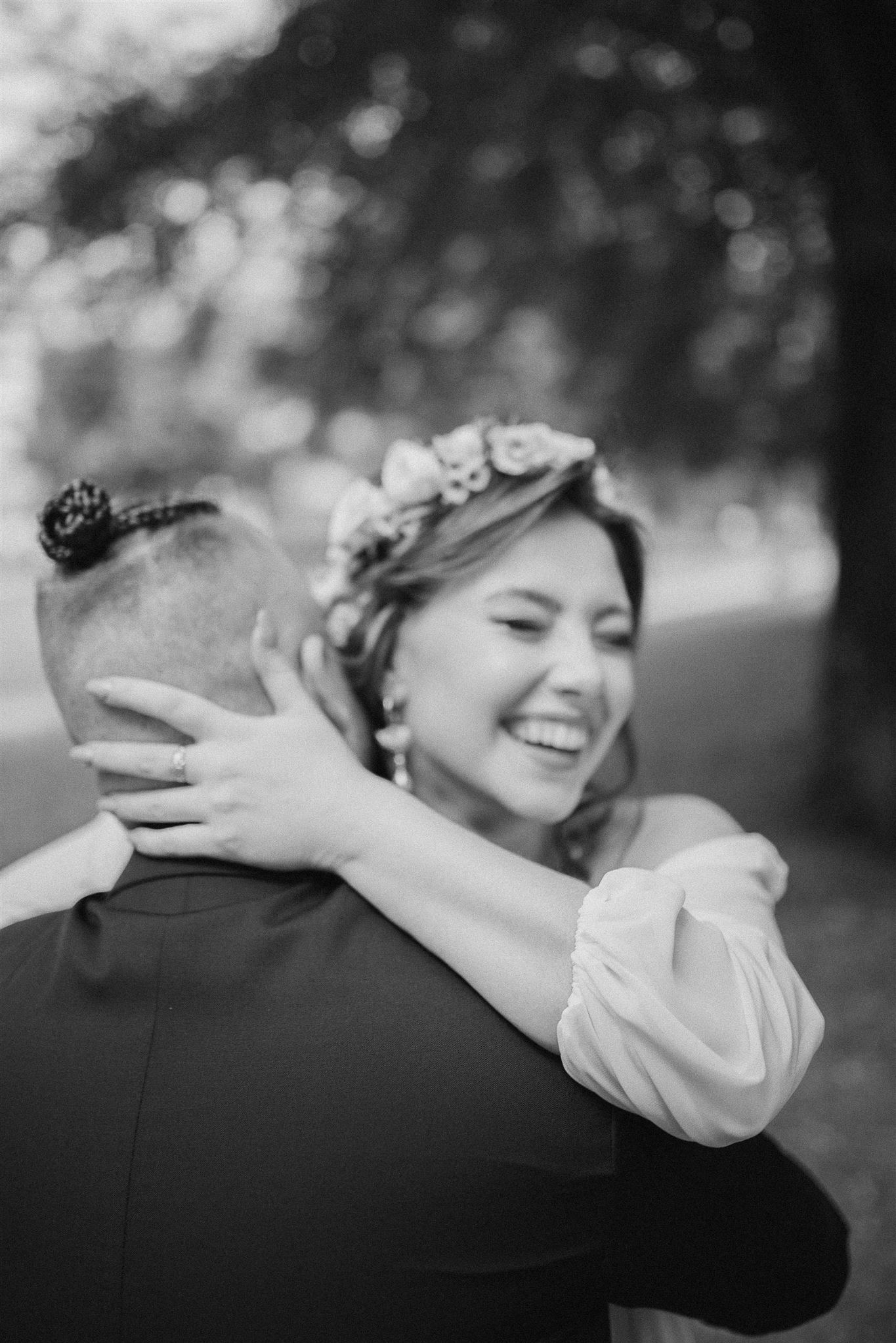 Czarno-białe zdjęcie z Białegostoku: Uśmiechnięta panna młoda w wianku obejmuje pana młodego, widoczny pierścionek zaręczynowy.