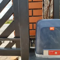 Szczegółowe zbliżenie na zamontowany napęd do bramy przesuwnej BFT Ultra z zębatą listwą, umieszczony obok murowanego słupka.