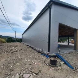 Nowoczesna hala magazynowa z płyt warstwowych w trakcie budowy, widok z zewnątrz, widoczne elementy konstrukcyjne i instalacje tymczasowe.