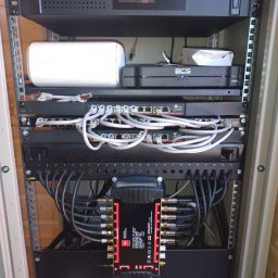 it4ti.pl - Szafa rack z zainstalowanymi urządzeniami: UPS Volt Polska, router WiFi, przełączniki sieciowe z podłączonymi kablami Ethernet, multiswitch z kablami koncentrycznymi, listwa zasilająca...