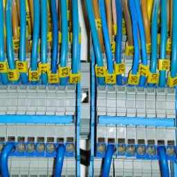 Szczegółowe ujęcie z bliska na panel sterowniczy z różnokolorowymi kablami oznaczonymi żółtymi numerowanymi etykietami, wpiętymi w szare i niebieskie złącza.