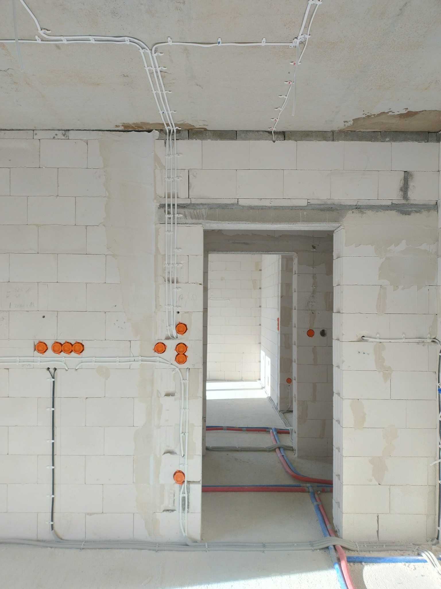 Wnętrze w stanie surowym z widocznymi instalacjami elektrycznymi w peszlach i puszkami podtynkowymi, oraz instalacją wodną w rurach PEX. Ściany z białego betonu komórkowego.