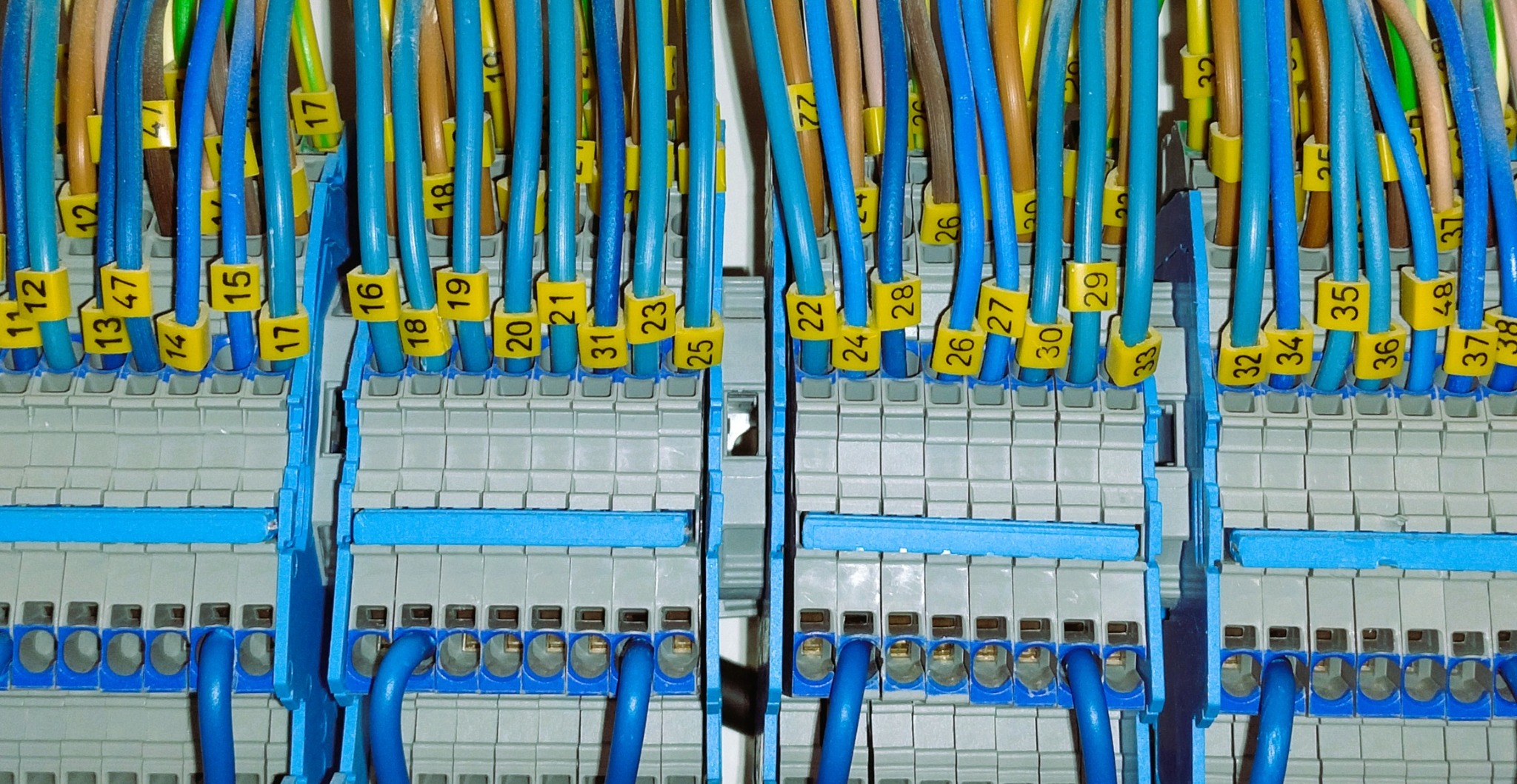 Szczegółowe ujęcie z bliska na panel sterowniczy z różnokolorowymi kablami oznaczonymi żółtymi numerowanymi etykietami, wpiętymi w szare i niebieskie złącza.