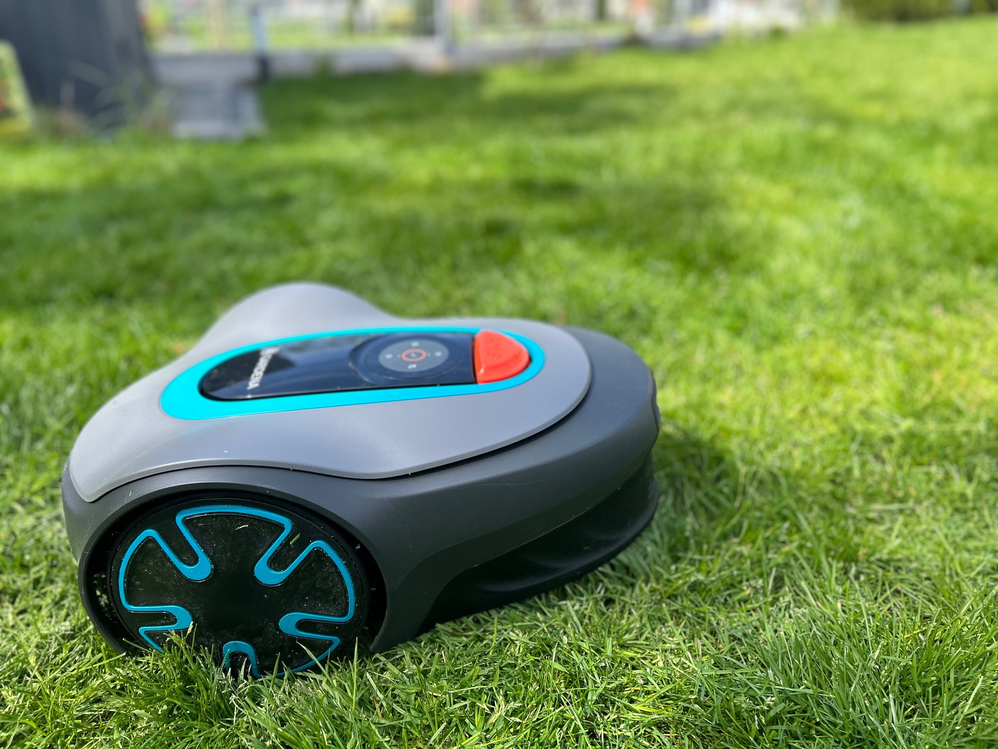 Szaro-turkusowy robot koszący Gardena leży na gęstej, zielonej trawie w słoneczny dzień.