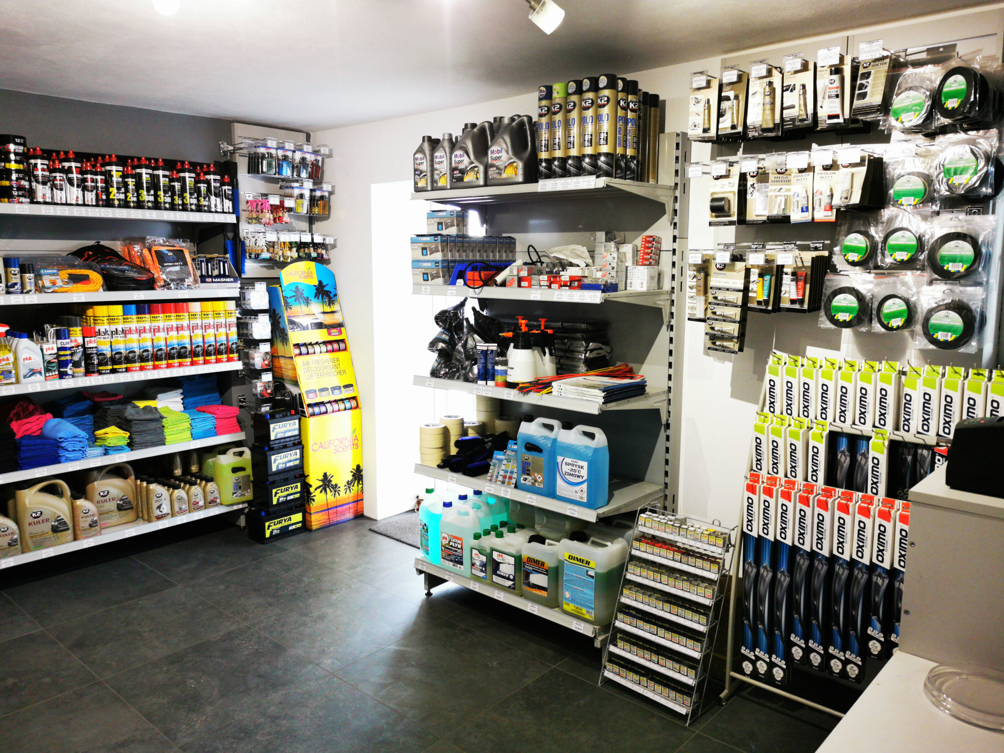 Wnętrze sklepu z artykułami motoryzacyjnymi i samochodowymi, regały wypełnione płynami eksploatacyjnymi, kosmetykami samochodowymi, wycieraczkami, olejami silnikowymi i innymi akcesoriami.